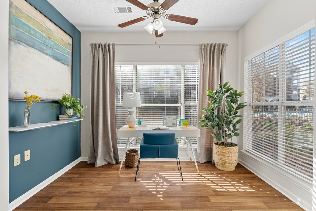 a home office with a large window and a ceiling fan