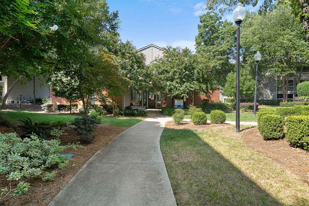 a sidewalk leading to a building with trees and bushes