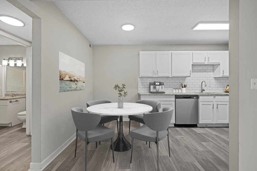 a dining area with a table and chairs and a kitchen in the background