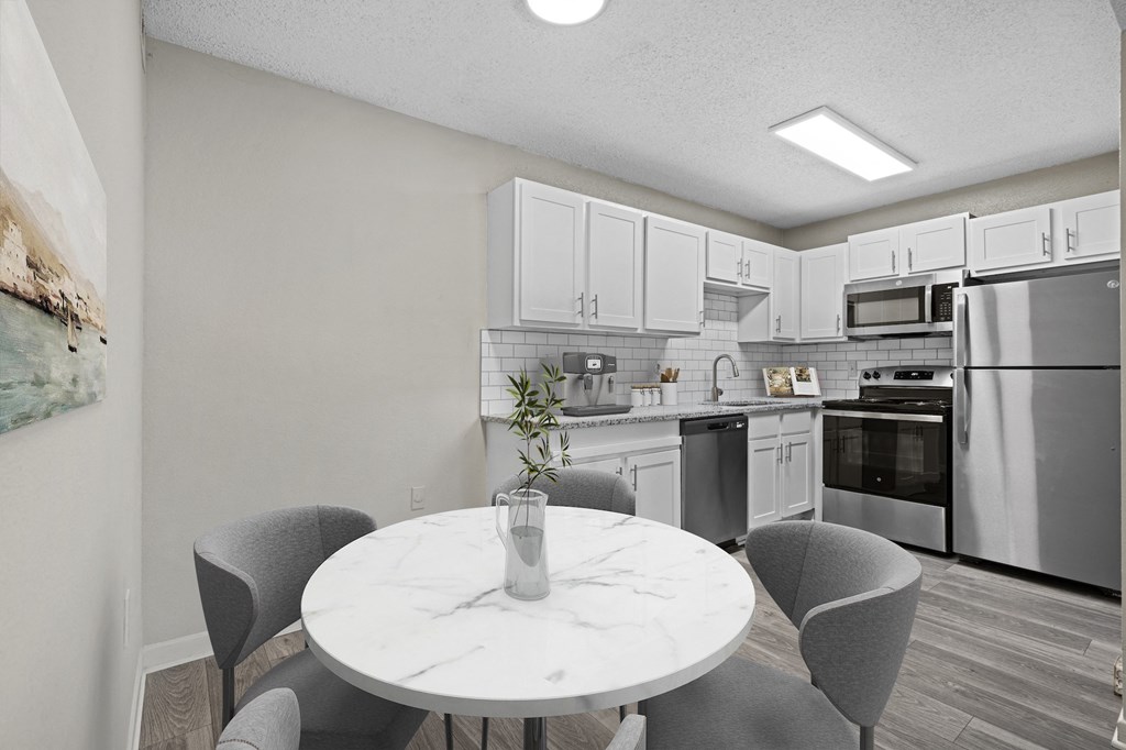 a kitchen with white cabinets and stainless steel appliances and a white marble table with four chairs