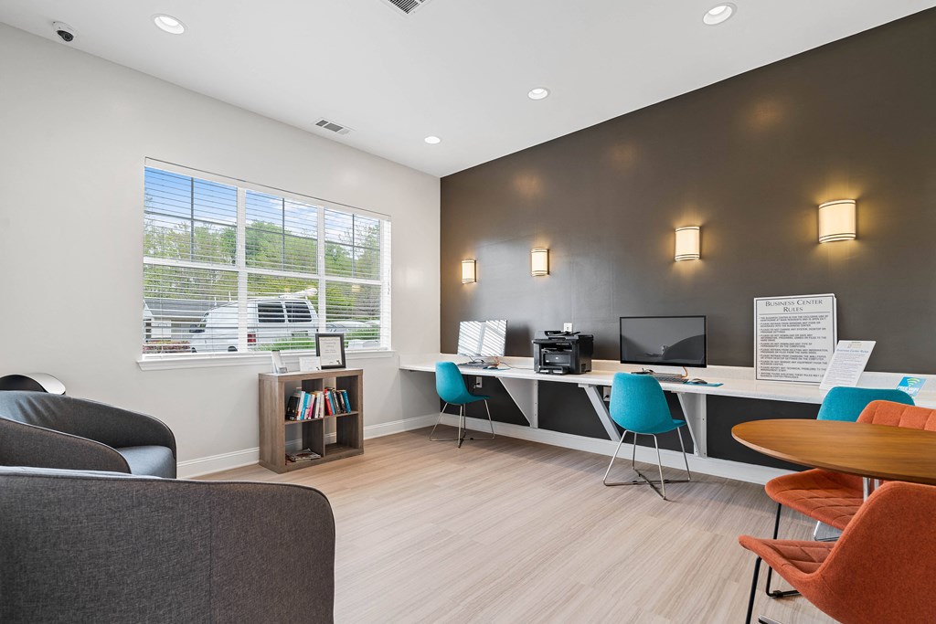 an office with chairs and a desk with a computer and a window