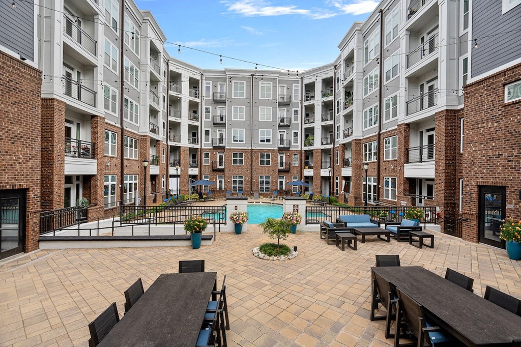 an open courtyard with picnic tables and a pool in front of an apartment building