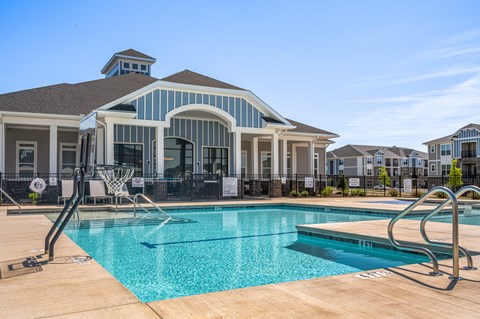 A swimming pool in front of a house with a basketball hoop.