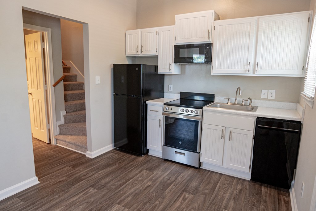 Spacious kitchen with white cabinetry,  black energy efficient appliances and plank style flooring