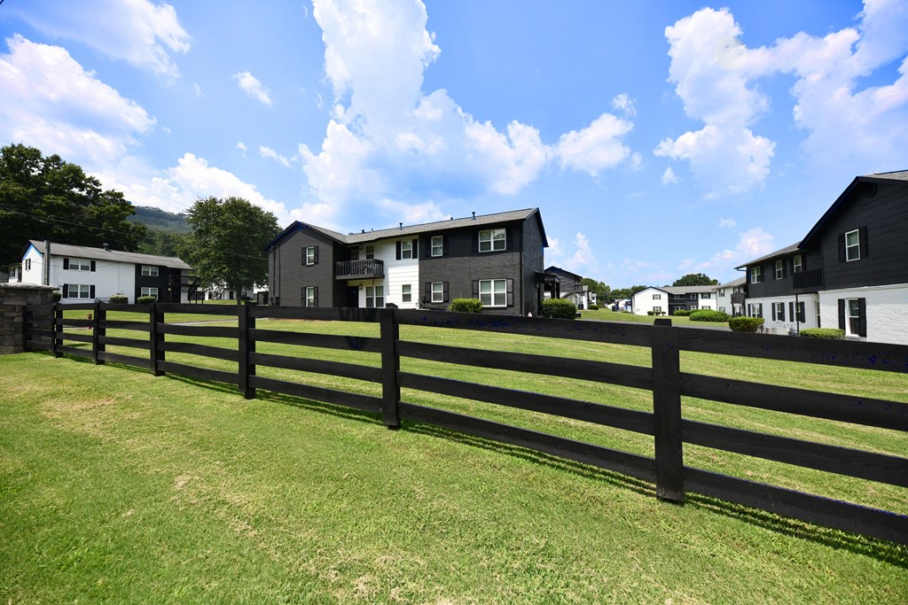 a black fence in front of a green field with houses in the background