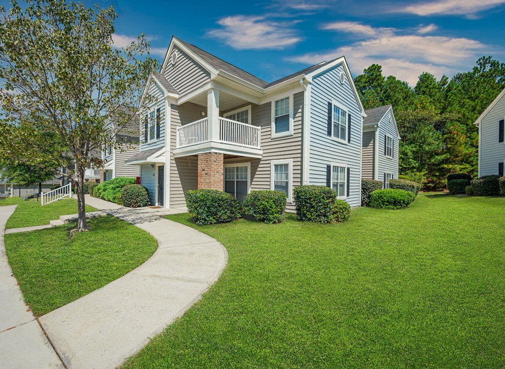a house with a walkway in front of a lawn and trees