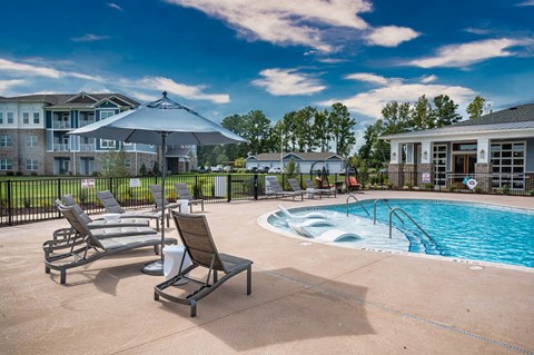 a pool with chairs and an umbrella next to an apartment building