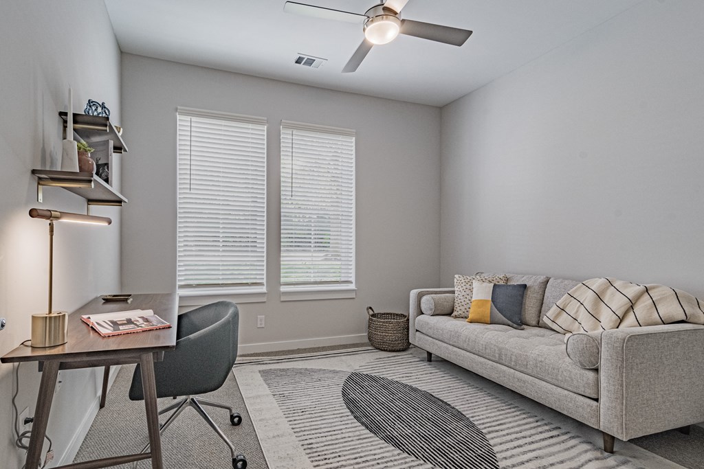a living room with a couch and a desk and a ceiling fan