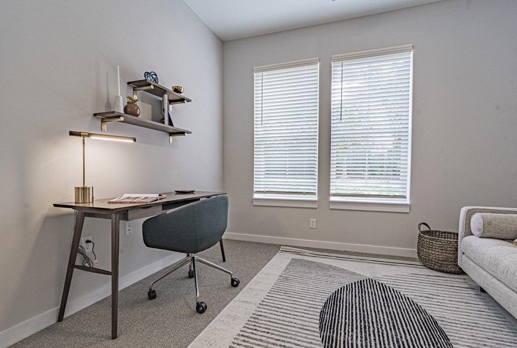 an office space with a desk and a chair and two windows