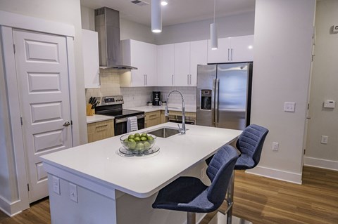 a kitchen with a large island with two blue chairs and a stainless steel refrigerator