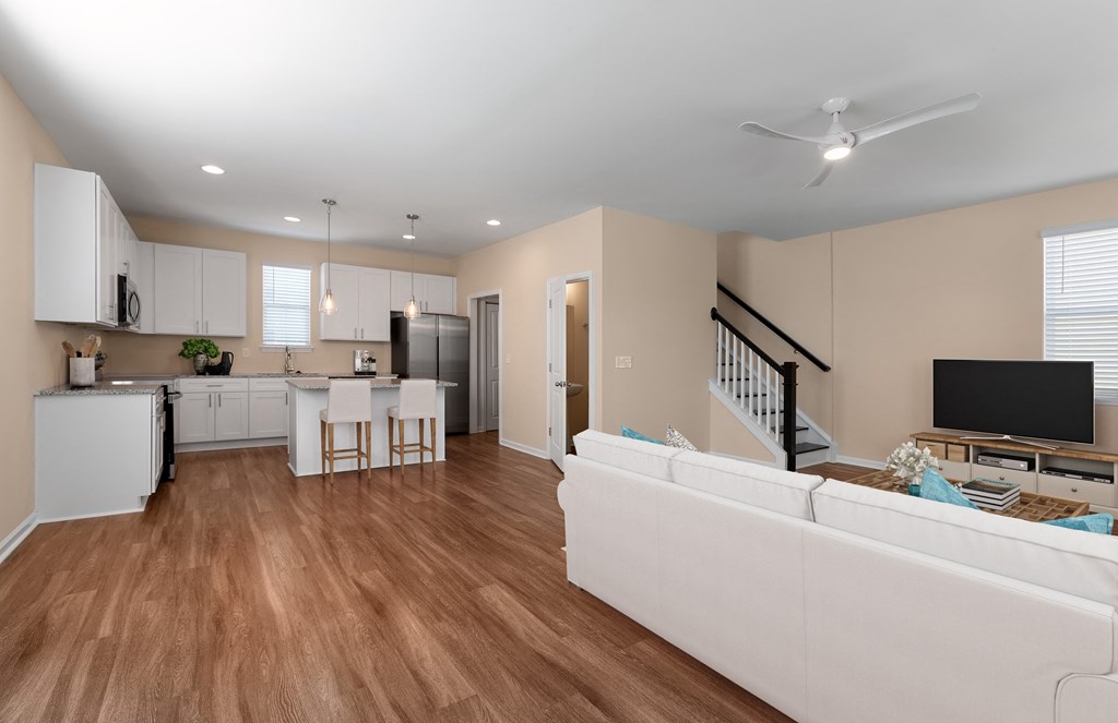 A living room with a white couch and a kitchen area with white cabinets.