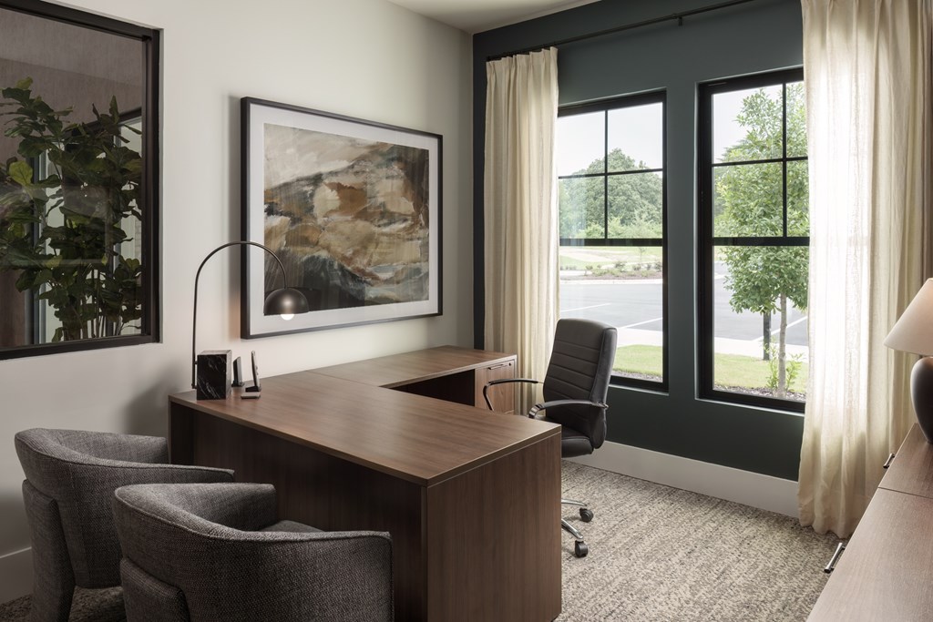 A room with a desk, chairs, and a painting on the wall.