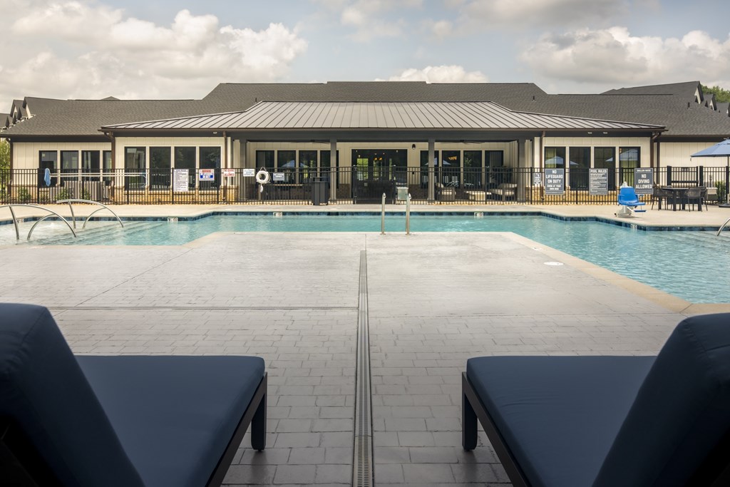 A pool area with a building in the background and two lounge chairs in the foreground.