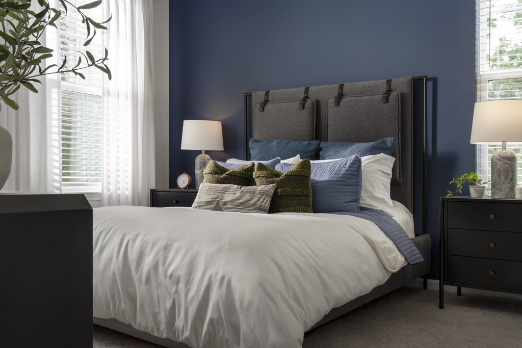A bed with a white comforter and a black headboard with a plant beside it.