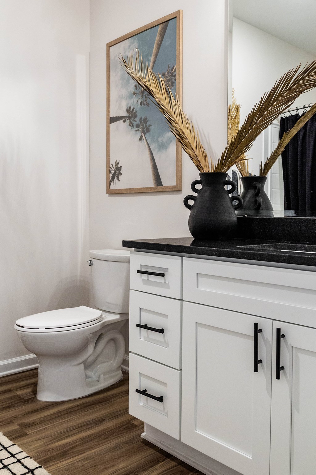 A bathroom with a toilet, a cabinet, and a painting on the wall. at Evolve Waterford Apartments in Belville, NC