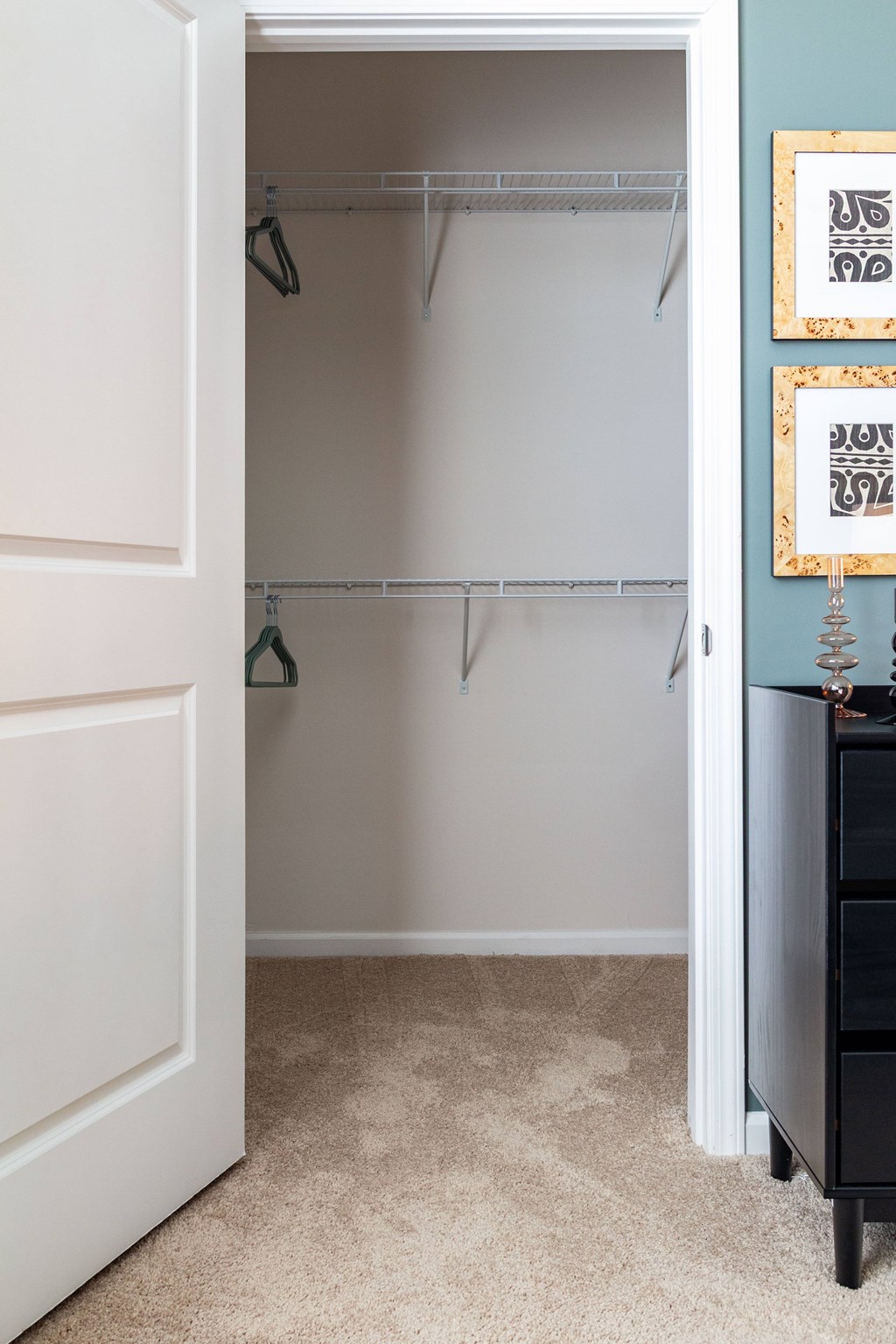 A white closet with a black dresser and two framed pictures on the wall. at Evolve Waterford Apartments in Belville, NC