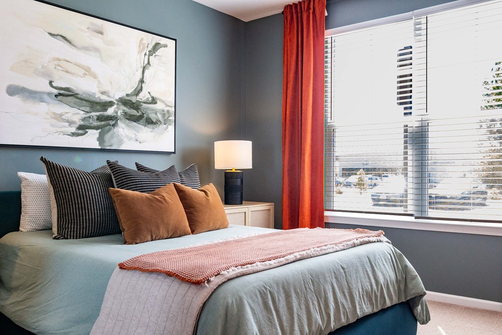 A bedroom with a large bed and a painting on the wall at Evolve Waterford Apartments in Belville, NC