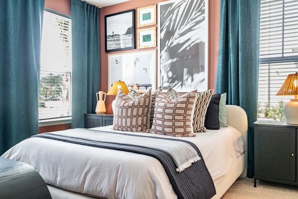 A bedroom with a large bed and a window with curtains at Evolve Waterford Apartments in Belville, NC