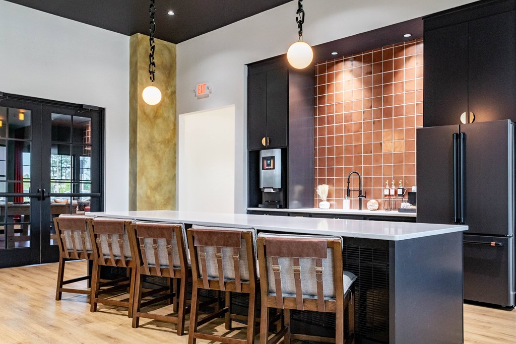 A clubhouse kitchen with a long island and chairs  at Evolve Waterford Apartments in Belville, NC