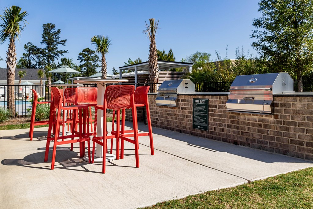 A set of red chairs are placed on a concrete  patio next to outdoor grills at Evolve Waterford Apartments in Belville, NC
