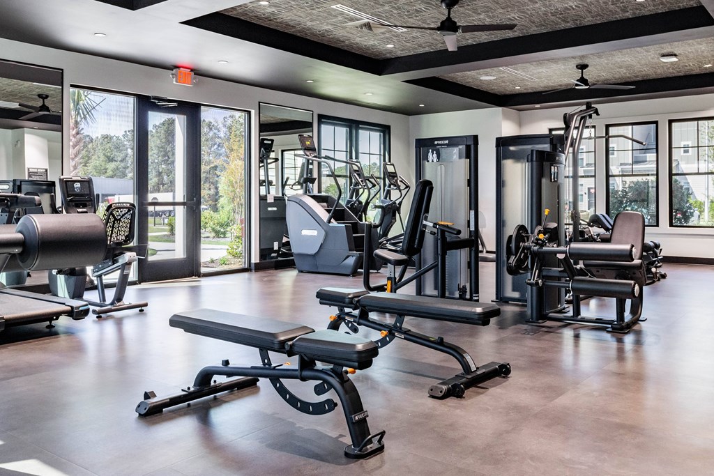 A gym with a variety of equipment including a bench press, a leg press, and a squat rack. at Evolve Waterford Apartments in Belville, NC