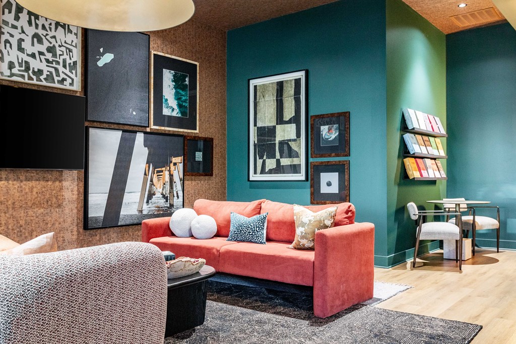 A seating area with a red couch and a grey chair at Evolve Waterford Apartments in Belville, NC