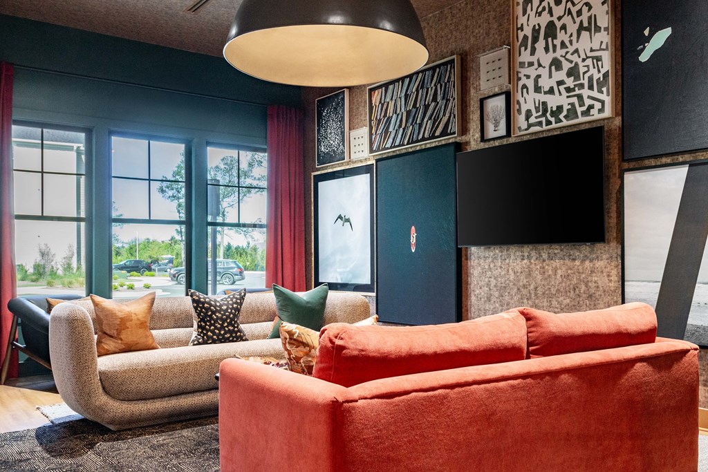 A  clubhouse with a red couch and a grey armchair at Evolve Waterford Apartments in Belville, NC.
