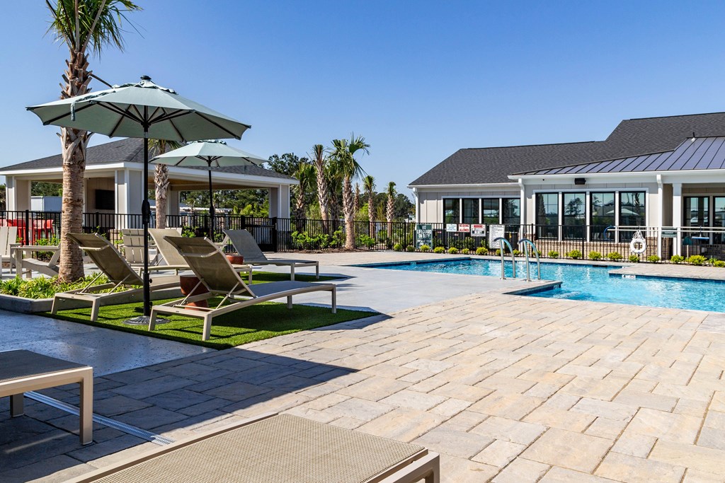 A pool area with a sun lounger and umbrella at Evolve Waterford Apartments in Belville, NC