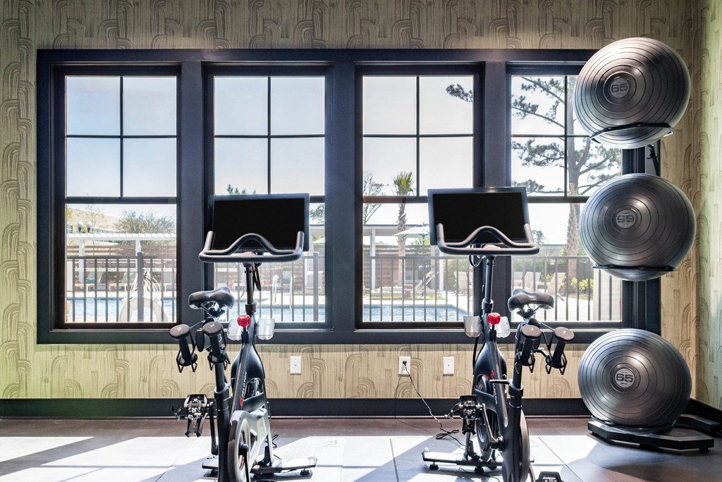 Two stationary bikes are in a room with a large window. at Evolve Waterford Apartments in Belville, NC