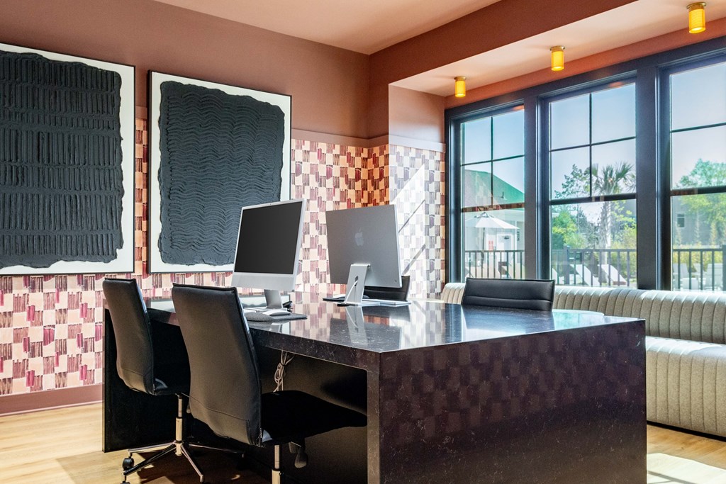 A black desk with two computers and two chairs in front of a window with a view of a green lawn at Evolve Waterford Apartments in Belville, NC.