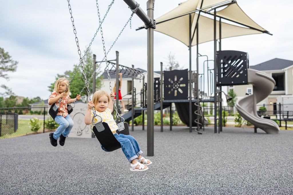 Two children playing on a swing set at a playground.