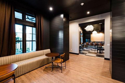 A modern living room with a large window and a dining area in the background.
