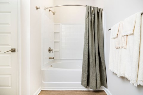 A white bathroom with a white tub and a grey shower curtain.