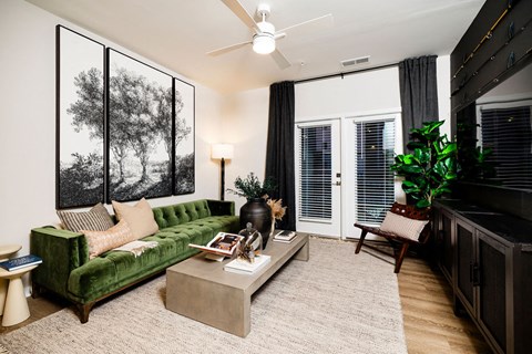A living room with a green couch, a coffee table, and a ceiling fan.