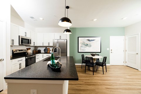 A kitchen with a black counter top and a dining table with chairs.