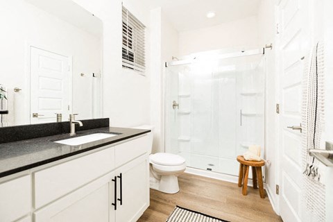 A white bathroom with a black counter top and a white toilet.