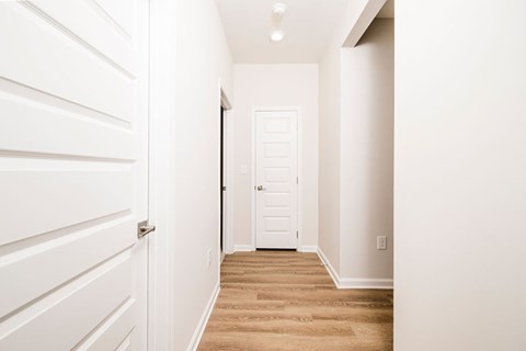 A hallway with a white door and a white wall.