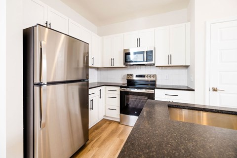 A kitchen with a stainless steel refrigerator and black countertops.