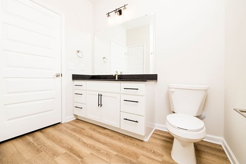 A white toilet sits in a bathroom with a white door and a mirror above a medicine cabinet.