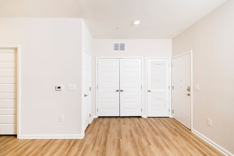 A room with white walls and wooden floors with a white door and three white closet doors.