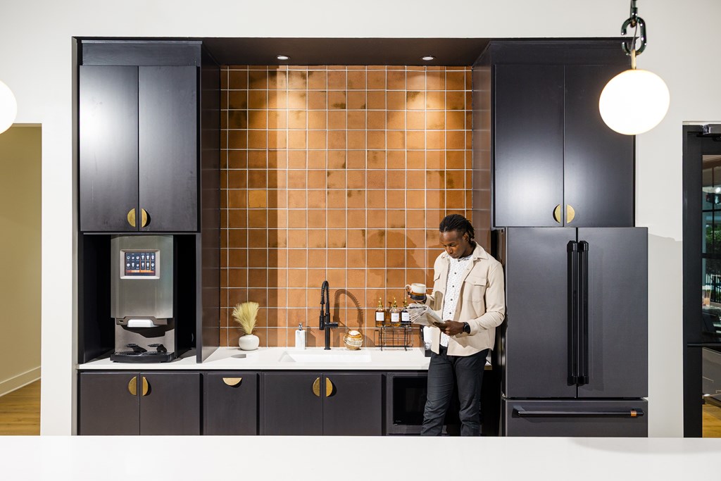 A man is standing in a kitchen with a black refrigerator and a coffee machine.