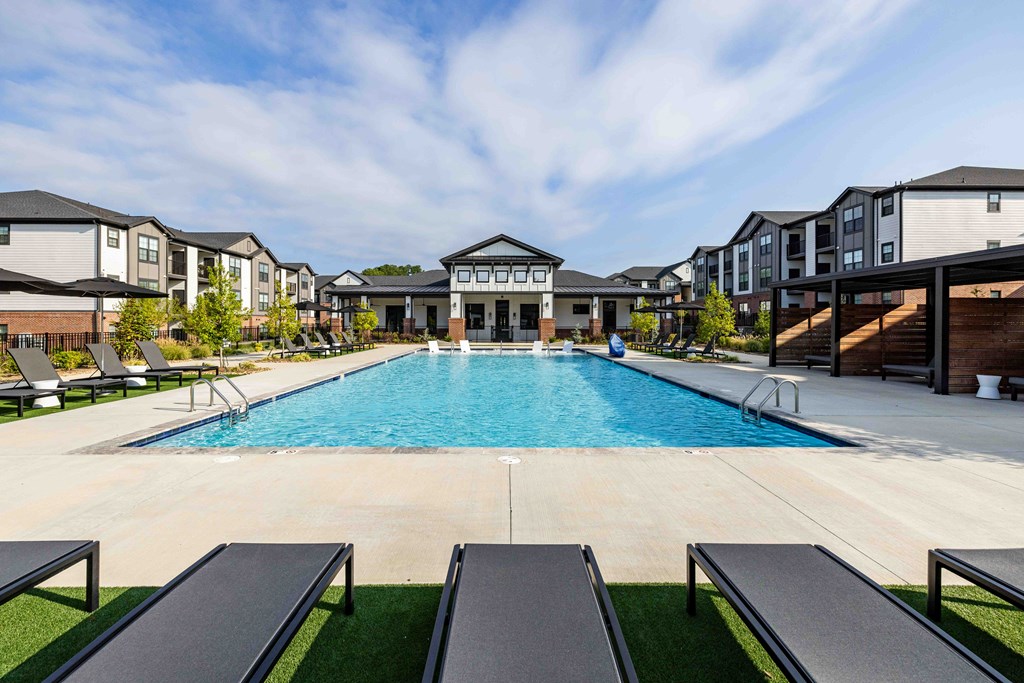 A large swimming pool surrounded by lounge chairs and apartment buildings.
