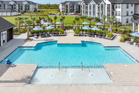 A large outdoor swimming pool surrounded by lounge chairs and umbrellas.
