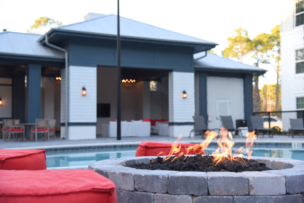 a fire pit in front of a pool with a pool house in the background