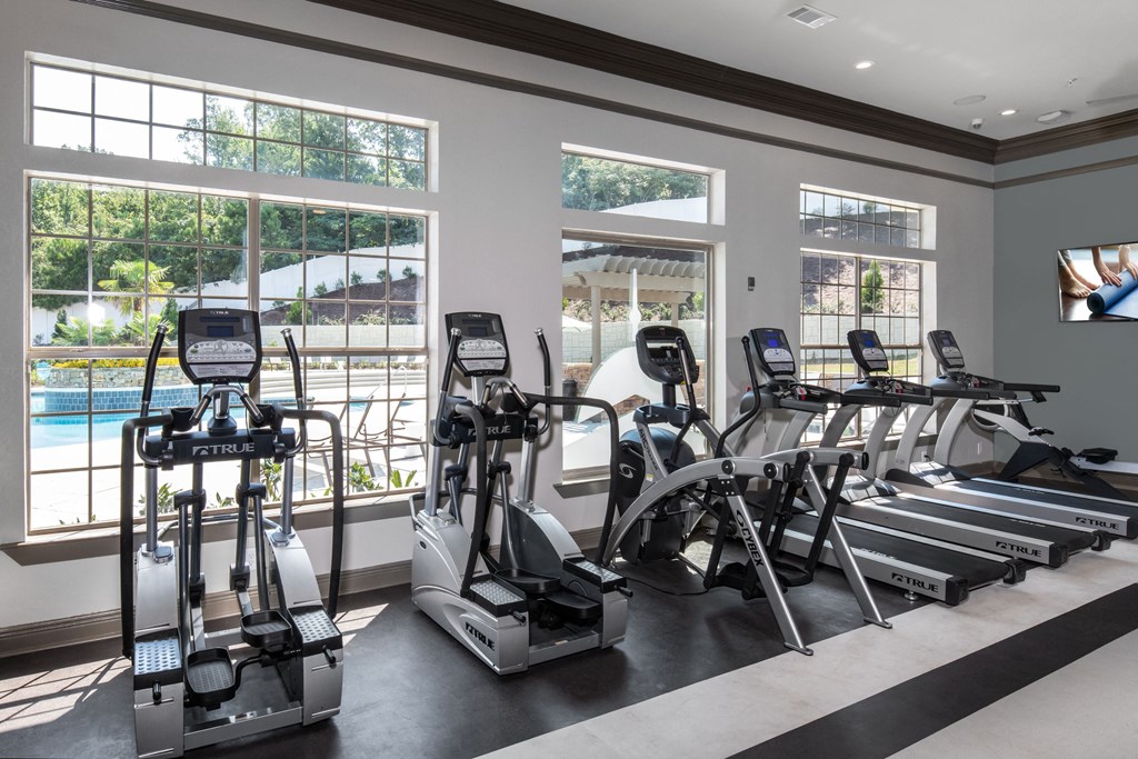 a gym with cardio machines and a pool in the background