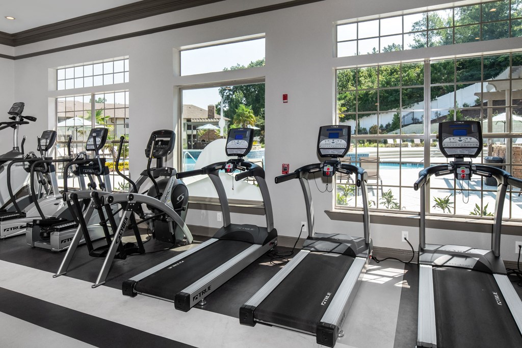 a gym with cardio equipment and windows overlooking a swimming pool