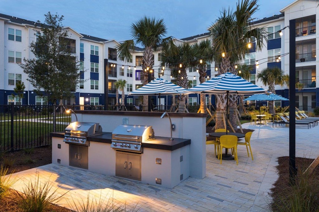 a patio with two bbq pits and umbrellas in an apartment complex