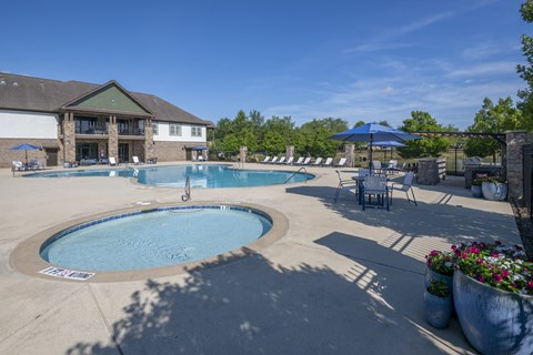A large outdoor swimming pool surrounded by a patio area with chairs and umbrellas.