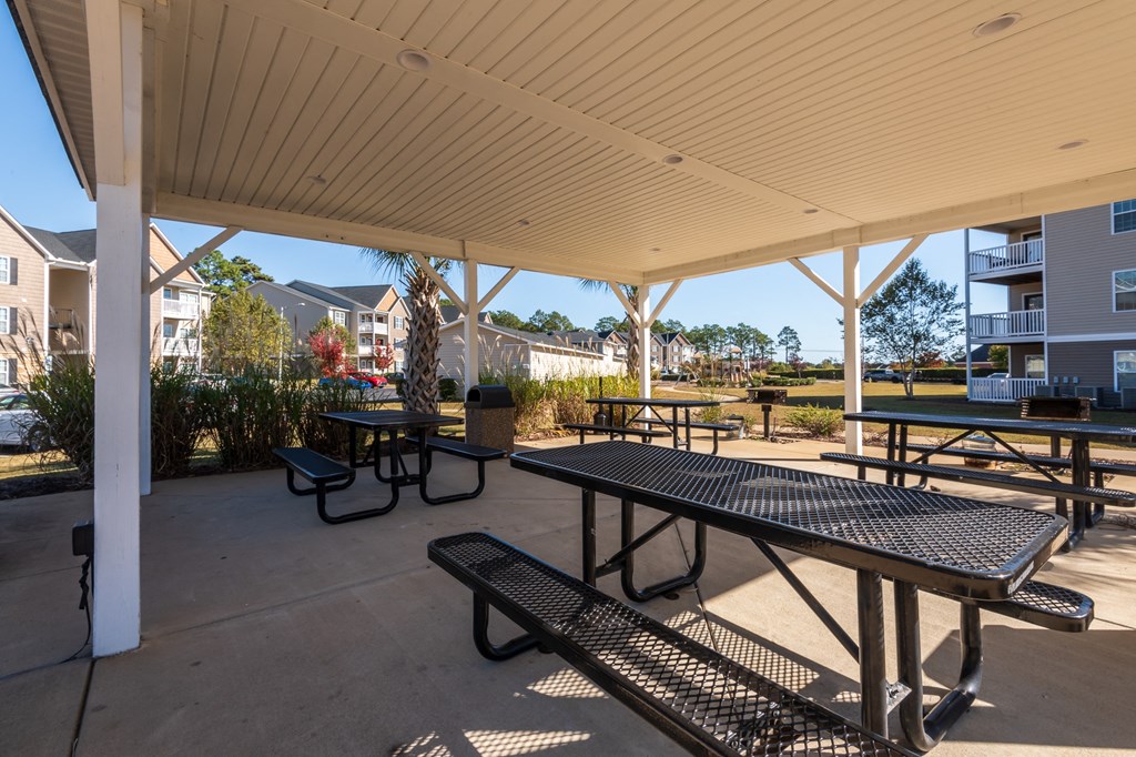 a covered picnic area with benches and tables in front of apartment buildings