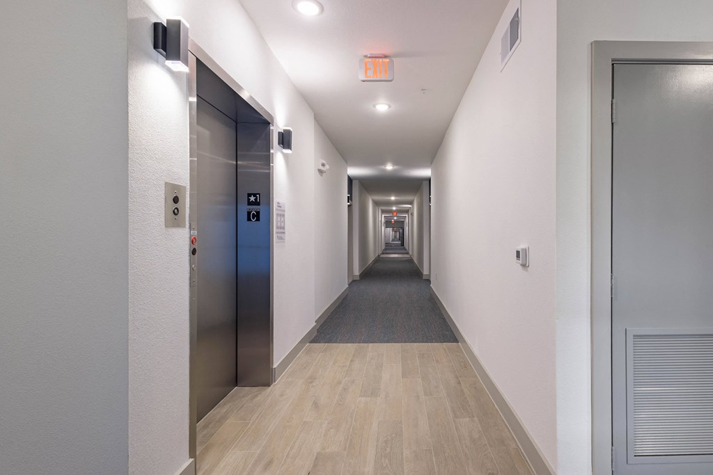 A long hallway with a red exit sign on the wall.